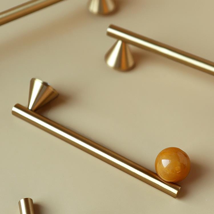 Poignées et boutons d'armoire Deauville de la marque Renfan, en métal brillant, fixés sur une porte en bois clair.